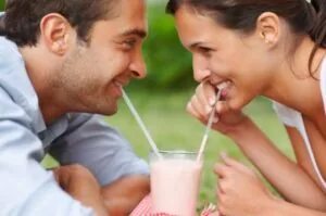 A man and woman drinking a milkshake, smiling at each other after whitening treatments in Logan.
